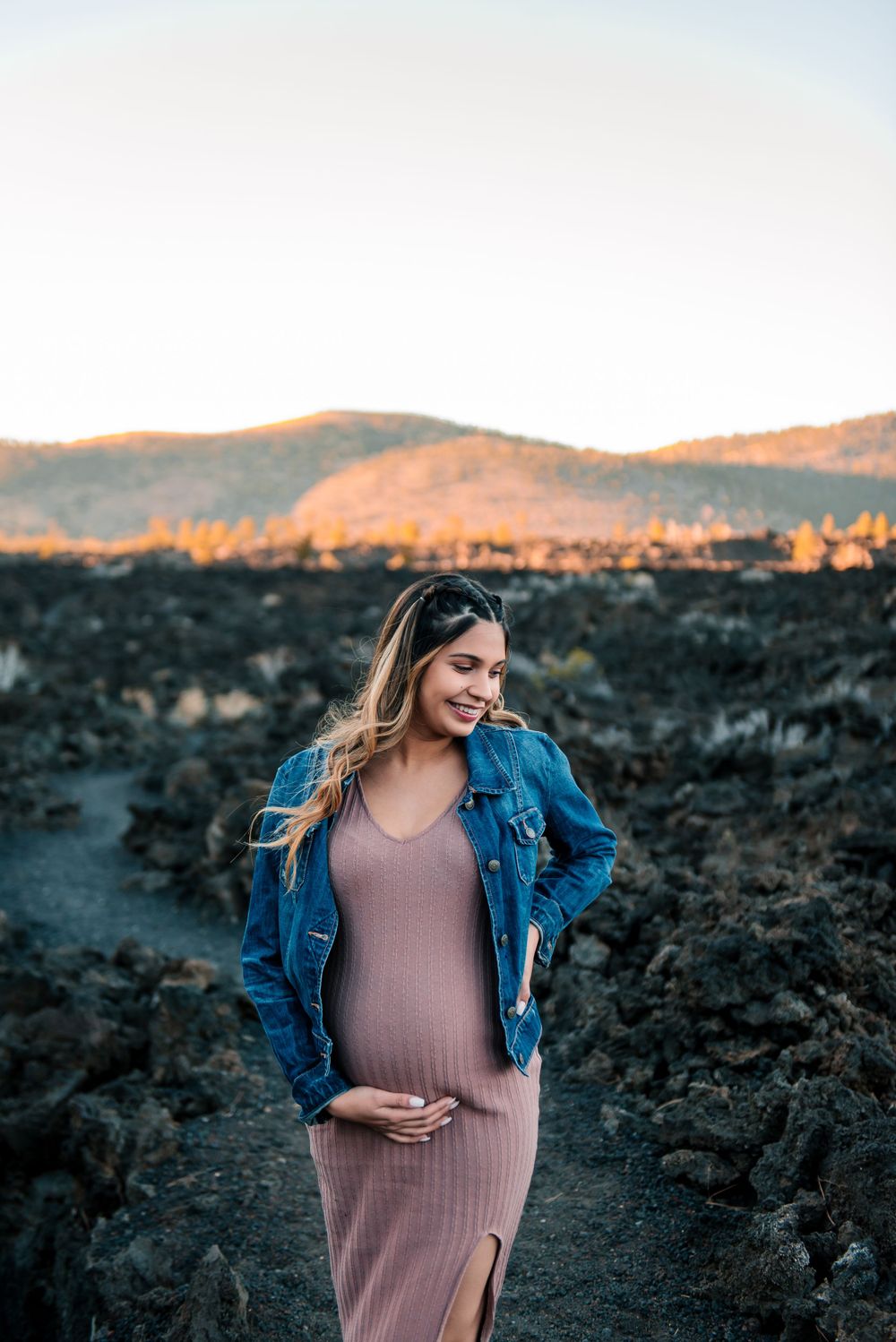 Maternity photos on rocky terrain with mountains and sunset in background.