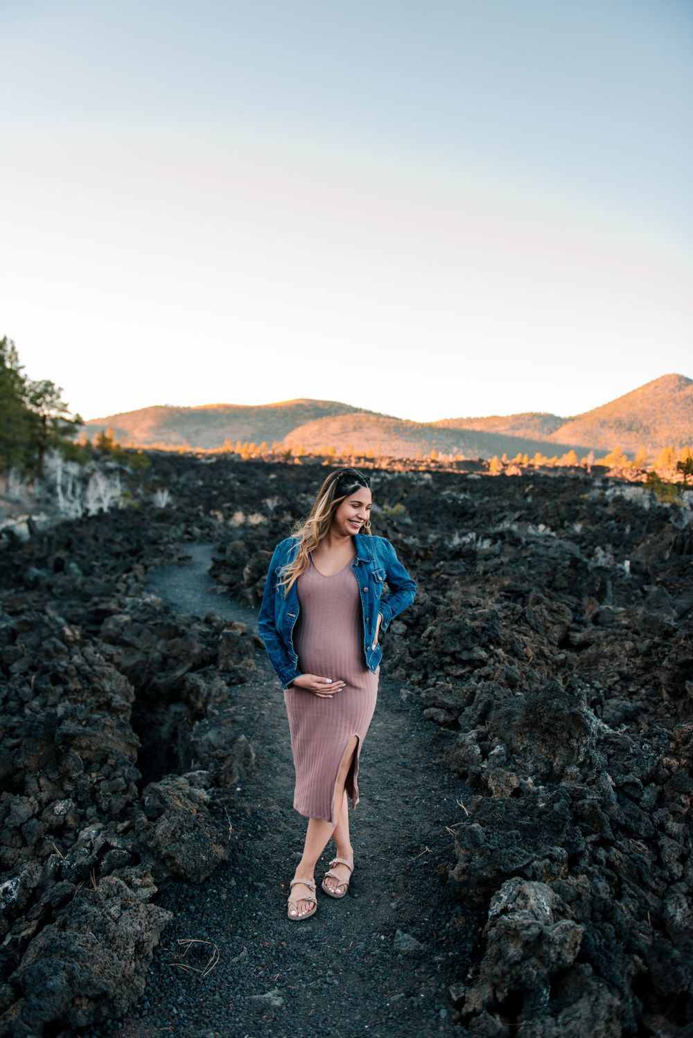 Expectant mother walks through volcanic landscape during sunset photoshoot.