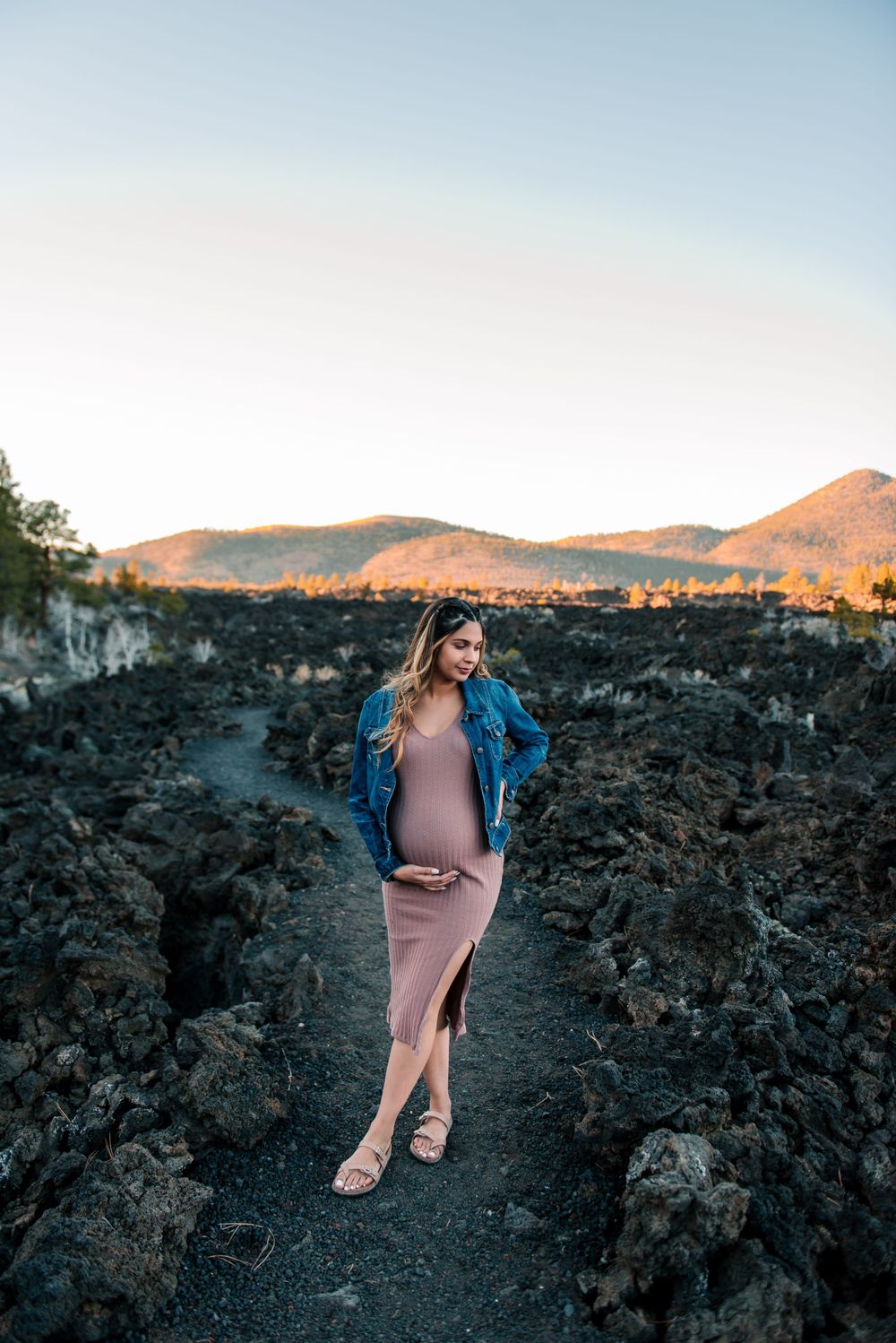 Maternity photoshoot on volcanic rocks with mountains glowing at sunset.