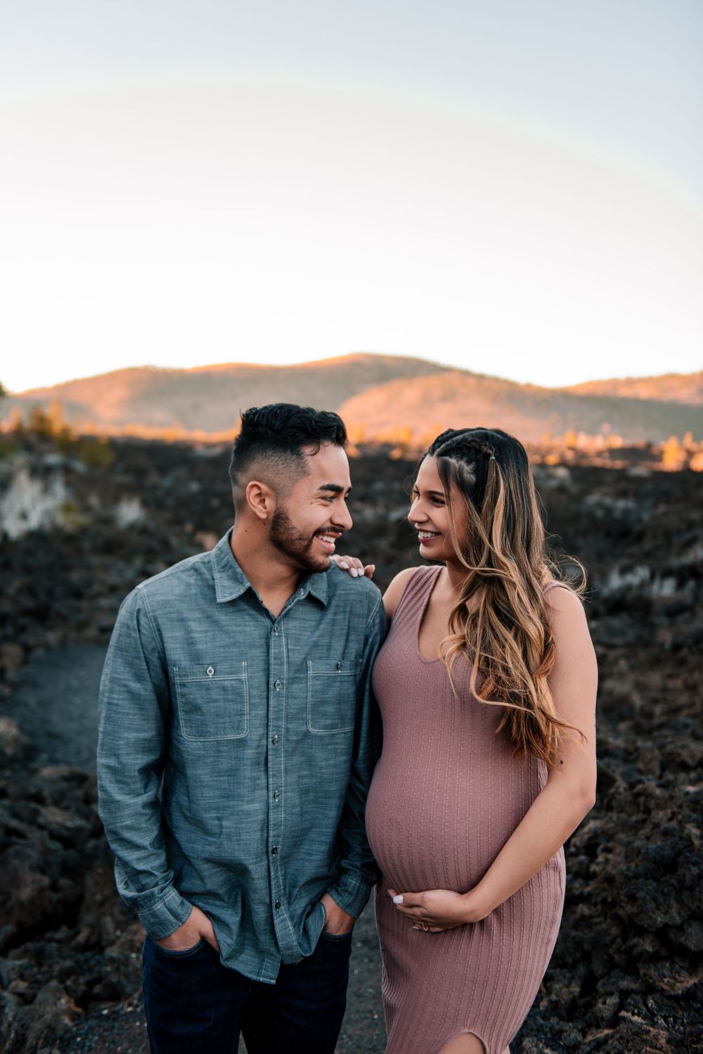 Happy couple laughing together during outdoor maternity session at sunset.