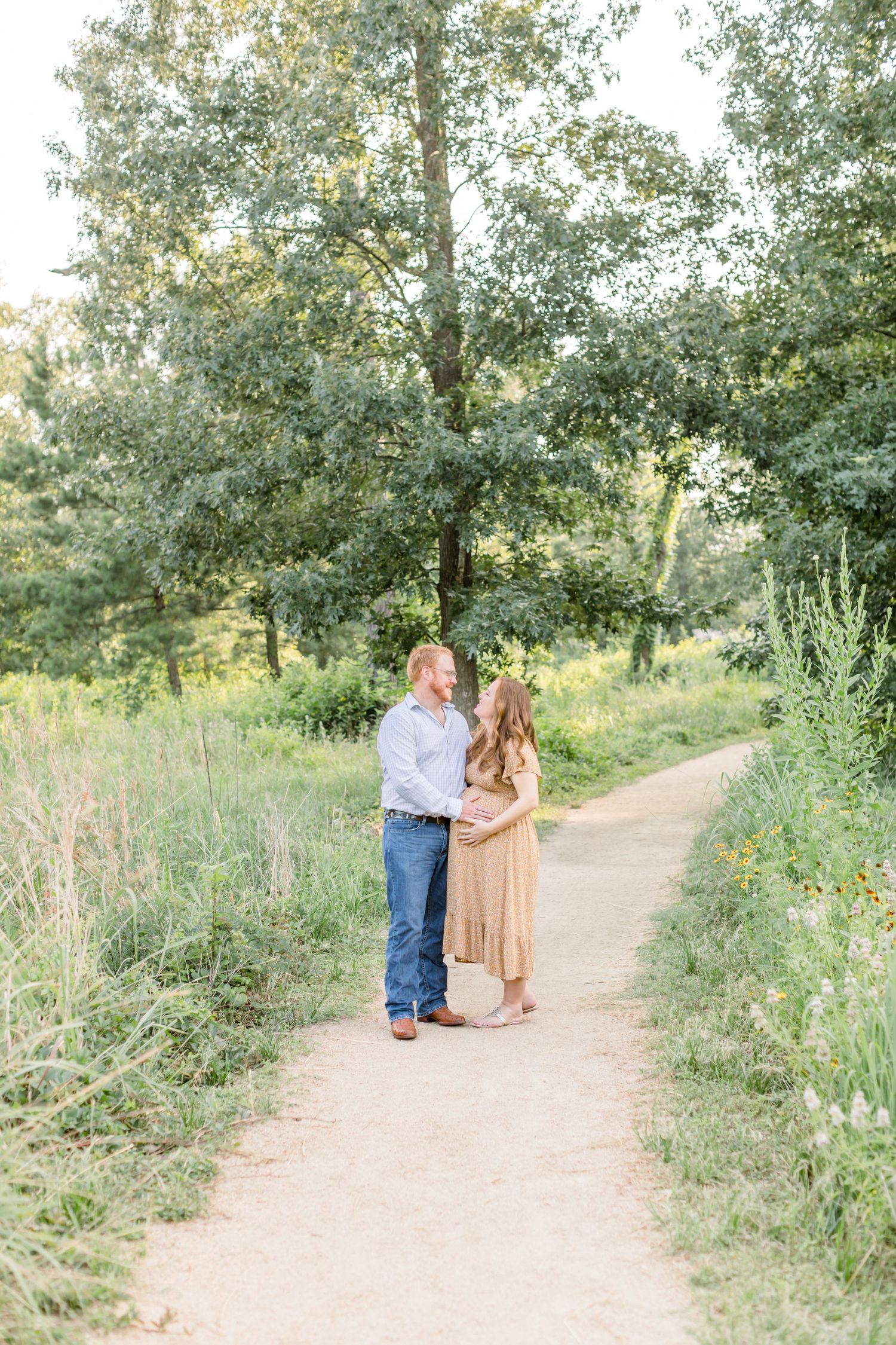 Couple shares romantic moment on wooded trail during maternity shoot.