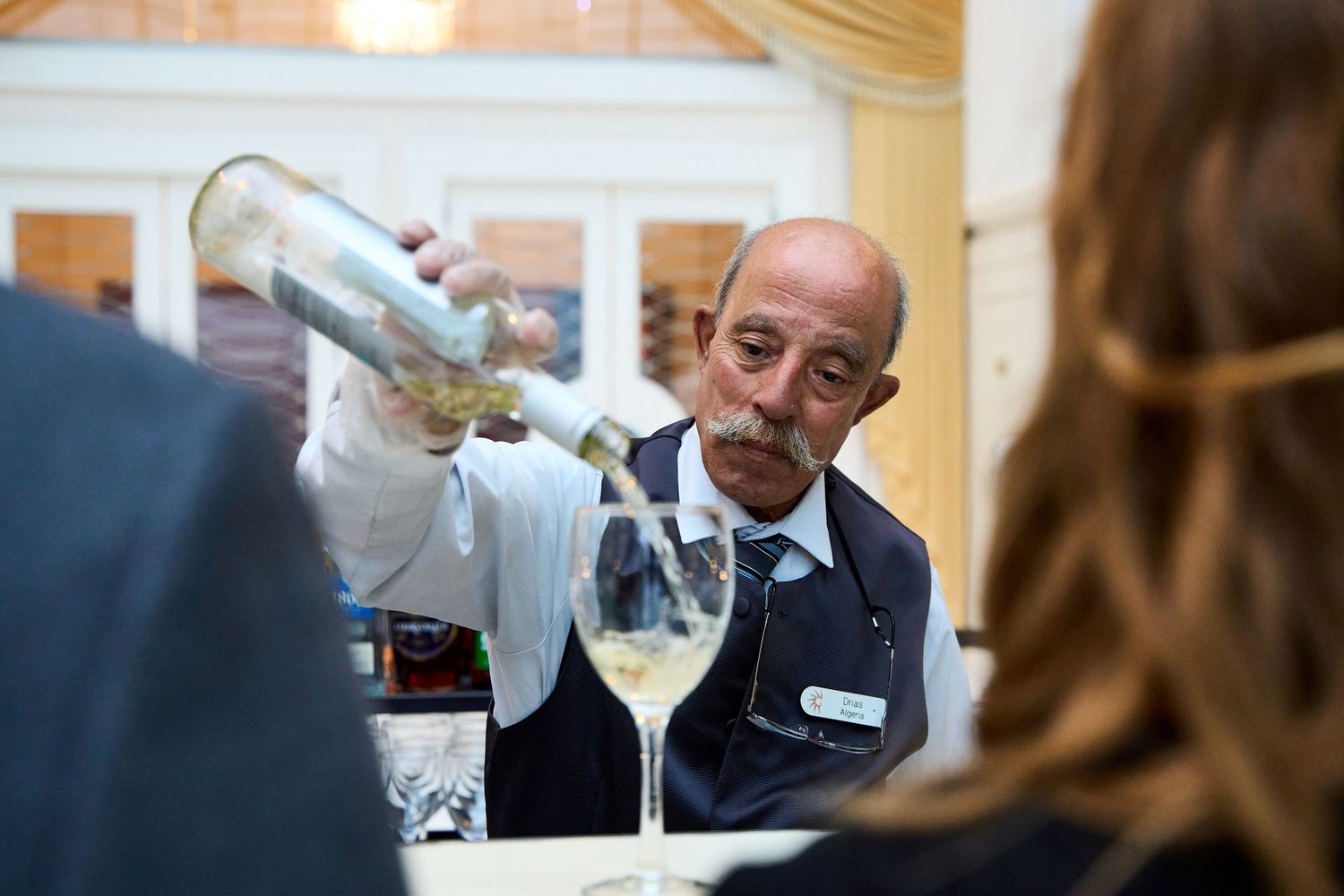 Professional waiter pouring white wine into a glass during upscale service.