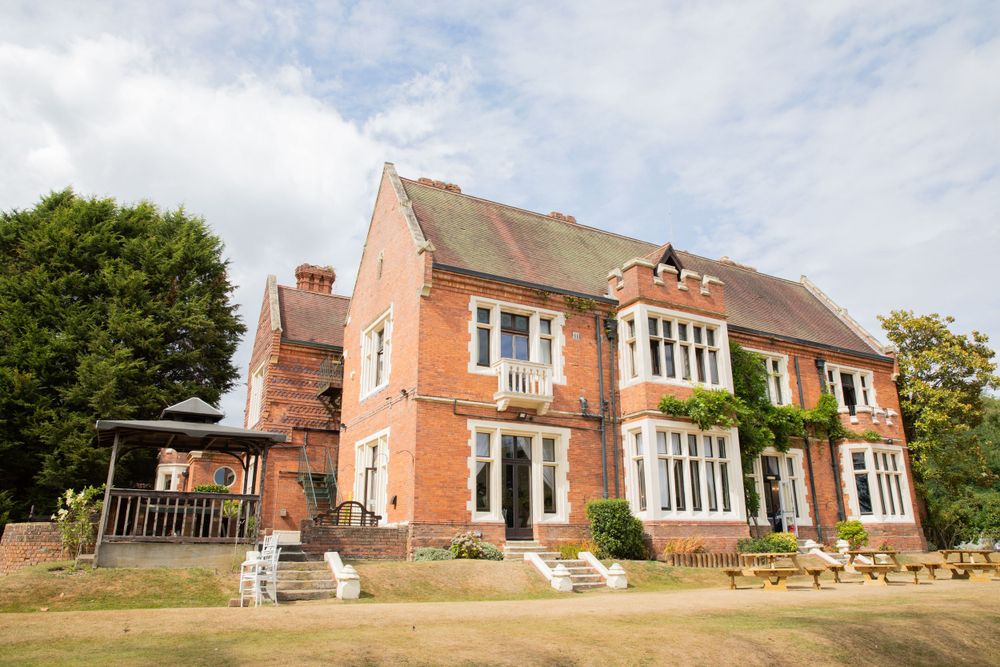 Large red brick country mansion with white trim on a sunny day with green lawn.