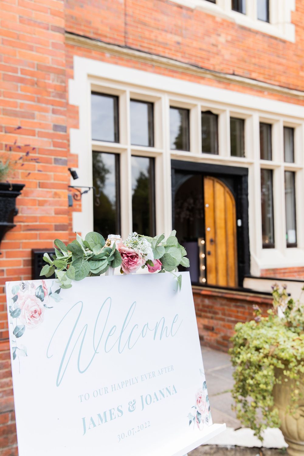 Welcome wedding sign with floral decoration outside brick building entrance.