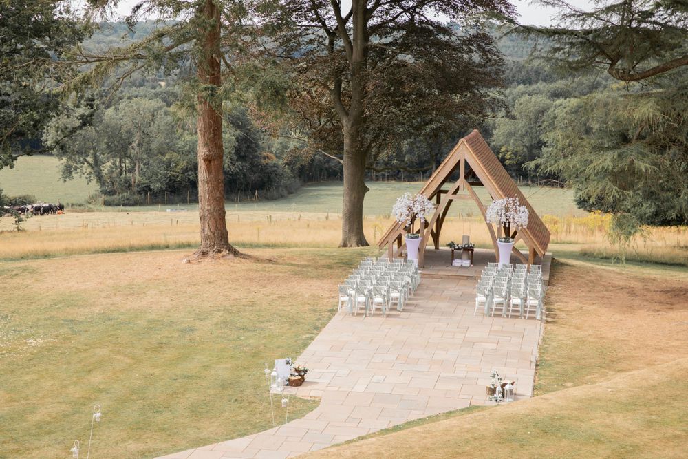 Outdoor wedding ceremony setup with wooden arch and white chairs in a forest setting.