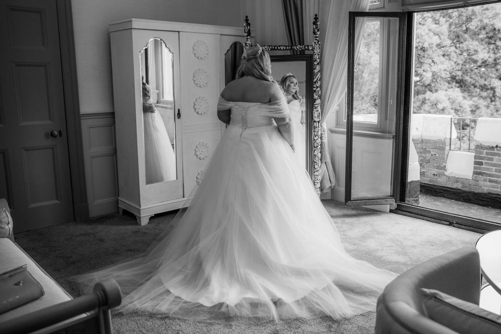Black and white photo of wedding dress preparation in elegant room with natural light.