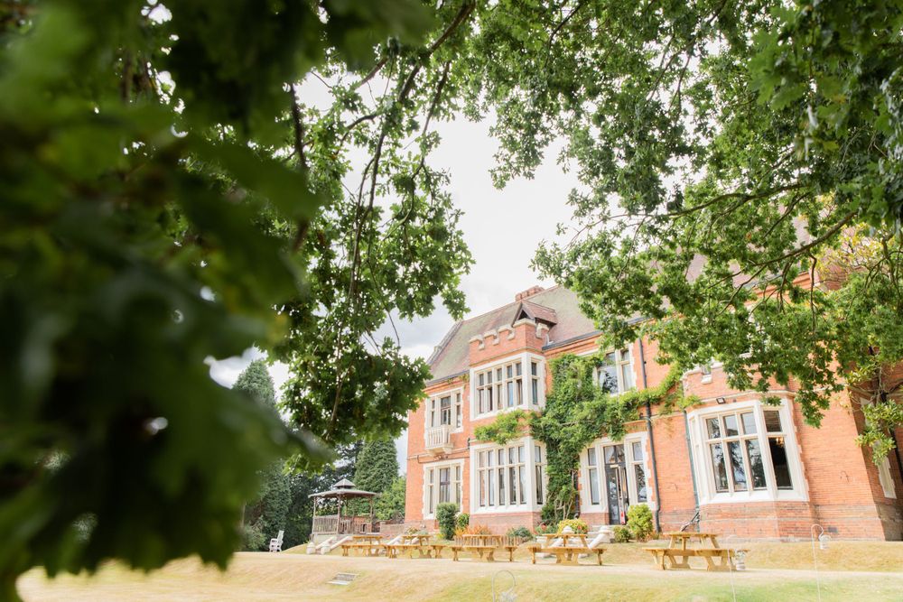 View of an elegant brick mansion through green summer foliage.