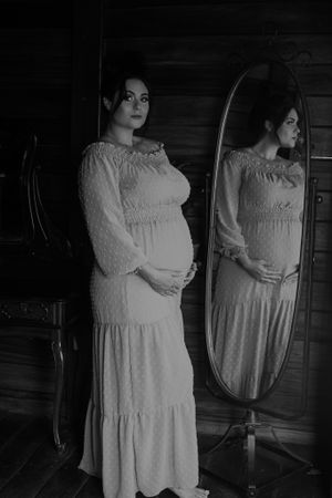 Classic black and white maternity portrait with vintage mirror reflection in a rustic wooden setting.