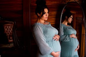 Dreamy maternity portrait in a powder blue dress with sheer sleeves against wooden walls.
