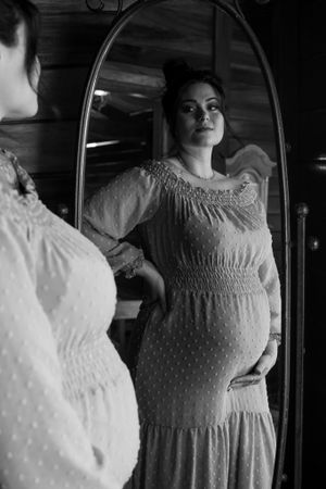 Artistic black and white maternity portrait with mirror reflection showing vintage dress details.