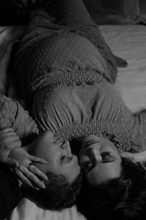 Intimate black and white maternity photo with couple lying down wearing matching dotted dresses.
