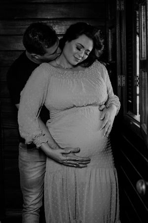 Tender black and white maternity moment captured against rustic wooden wall background.