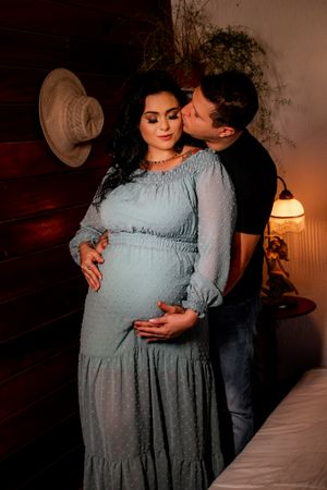 Romantic maternity portrait in blue dress with warm lighting and rustic wooden wall backdrop.