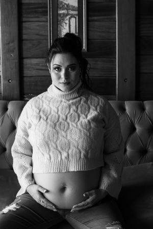 Black and white maternity photo featuring a white cable knit cropped sweater against a tufted sofa.