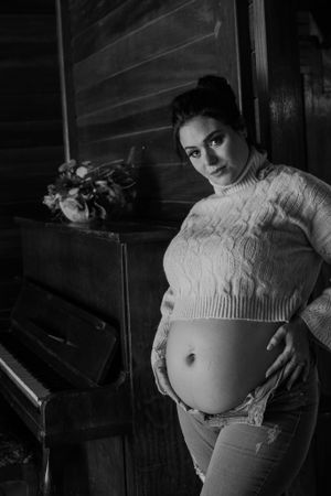 Artistic black and white maternity portrait with vintage piano and floral decor.