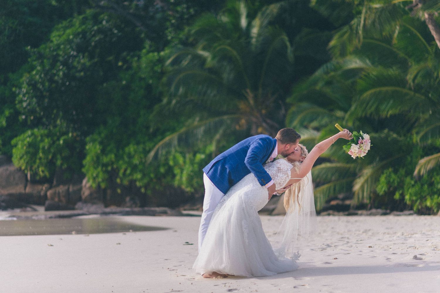 Couple enjoying a playful moment on a white sandy beach surrounded by palm trees.