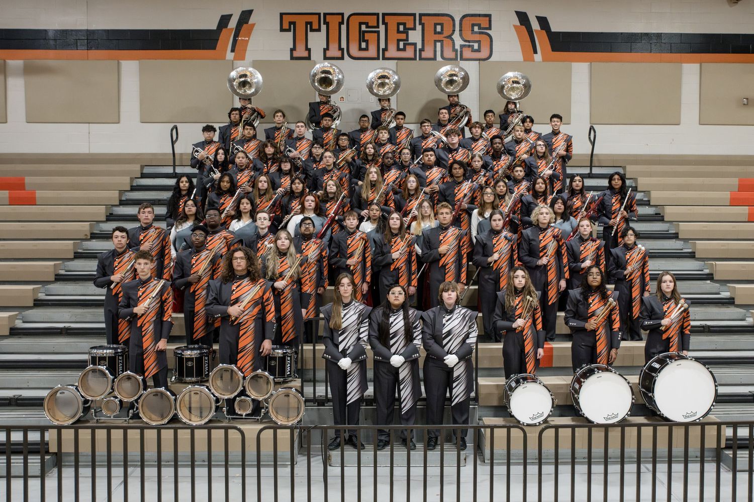 High school marching band members in uniform posed for traditional group photo on bleachers.