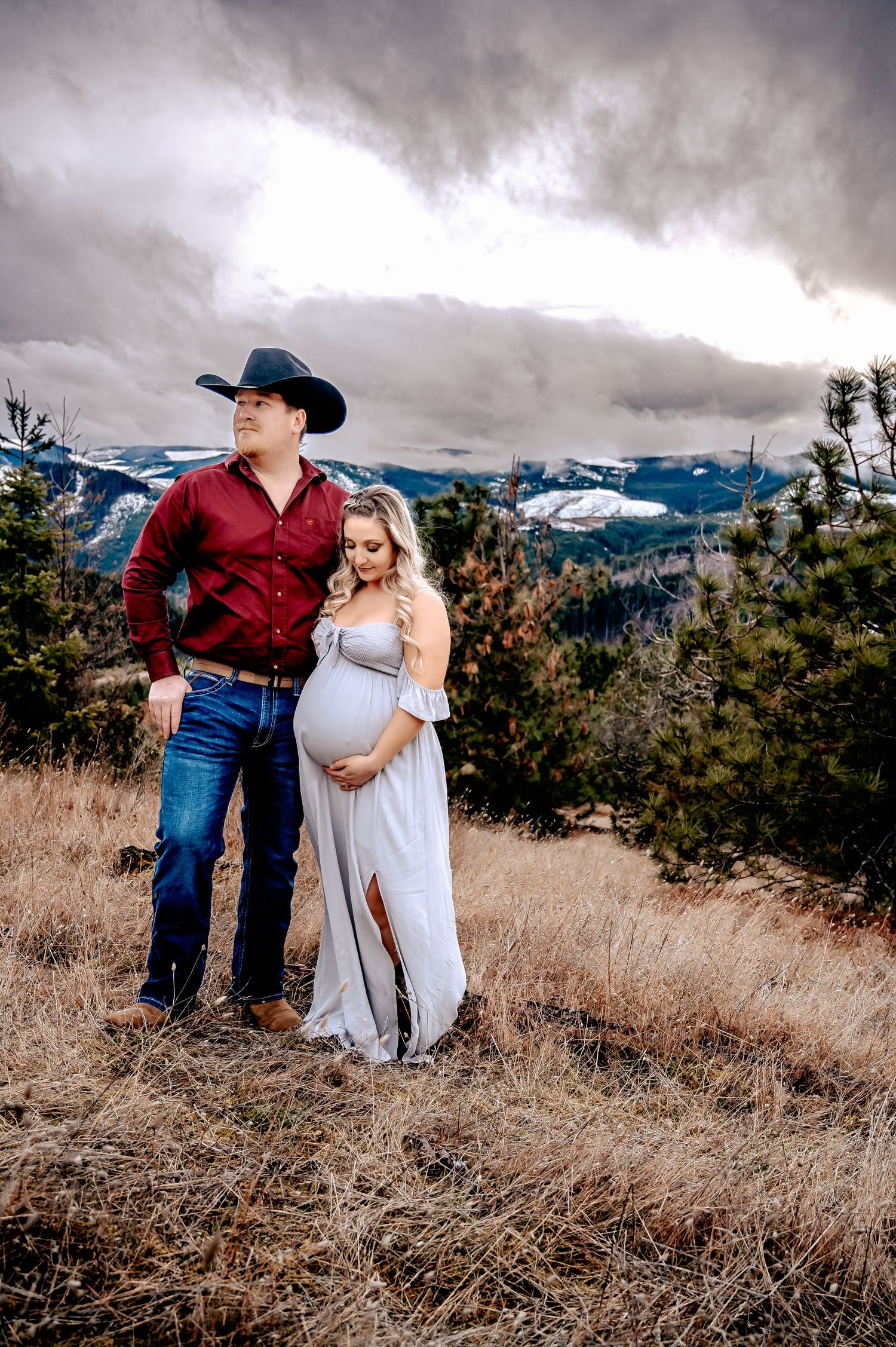 Dramatic mountain landscape serves as backdrop for an outdoor maternity photoshoot at sunset.