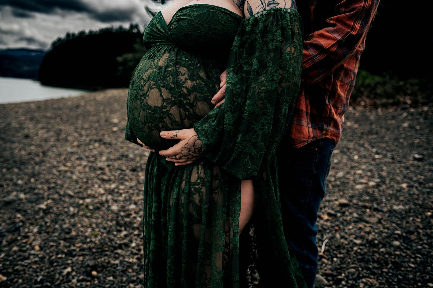 Couple embracing on a rocky beach with emerald green dress flowing in the wind.