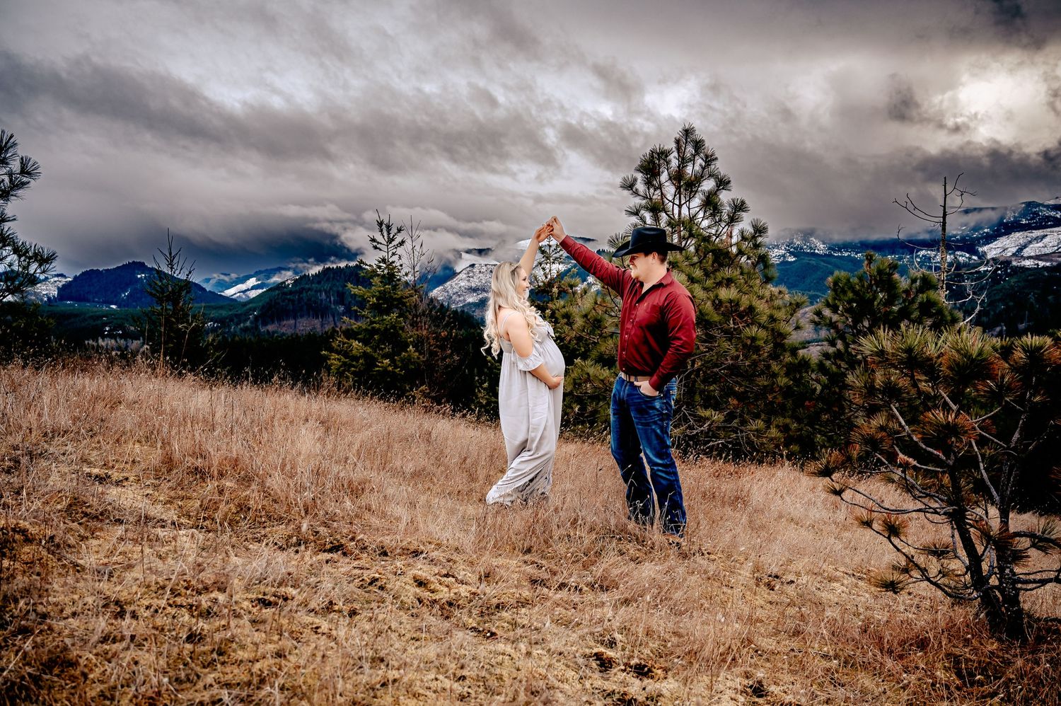 People walking through golden grass field with snow-capped mountains in background.