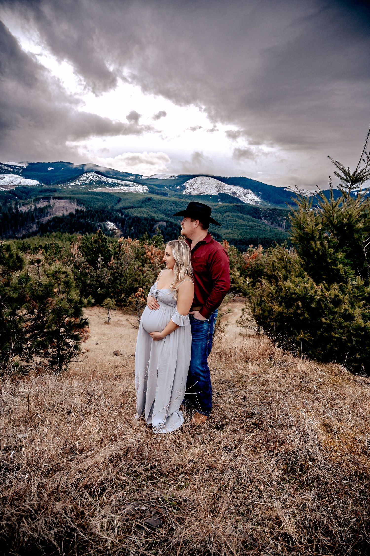 Couple in a mountain meadow with snow-capped peaks and dramatic storm clouds in background.