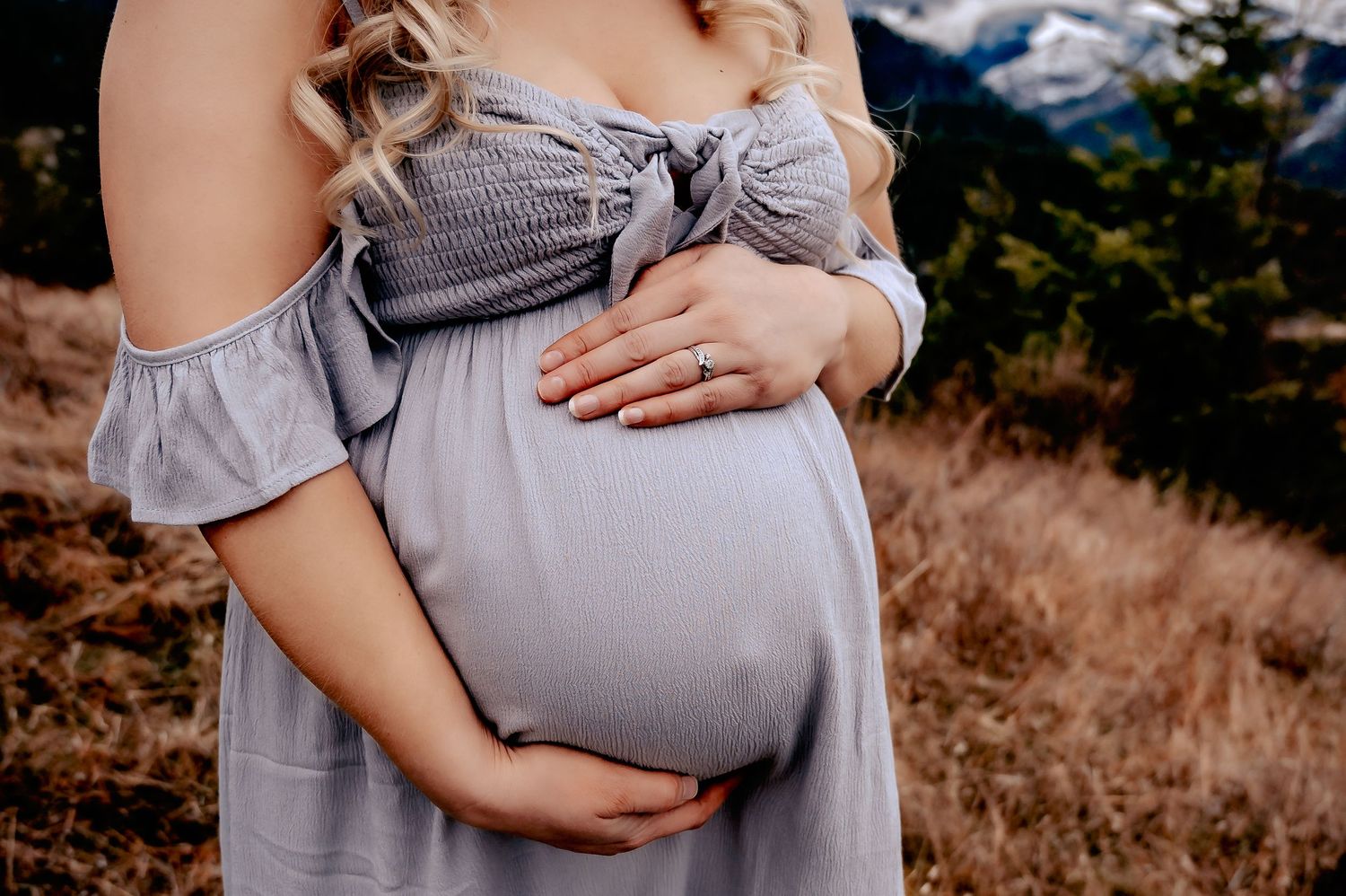 Light gray maternity dress silhouetted against mountain backdrop during sunset.