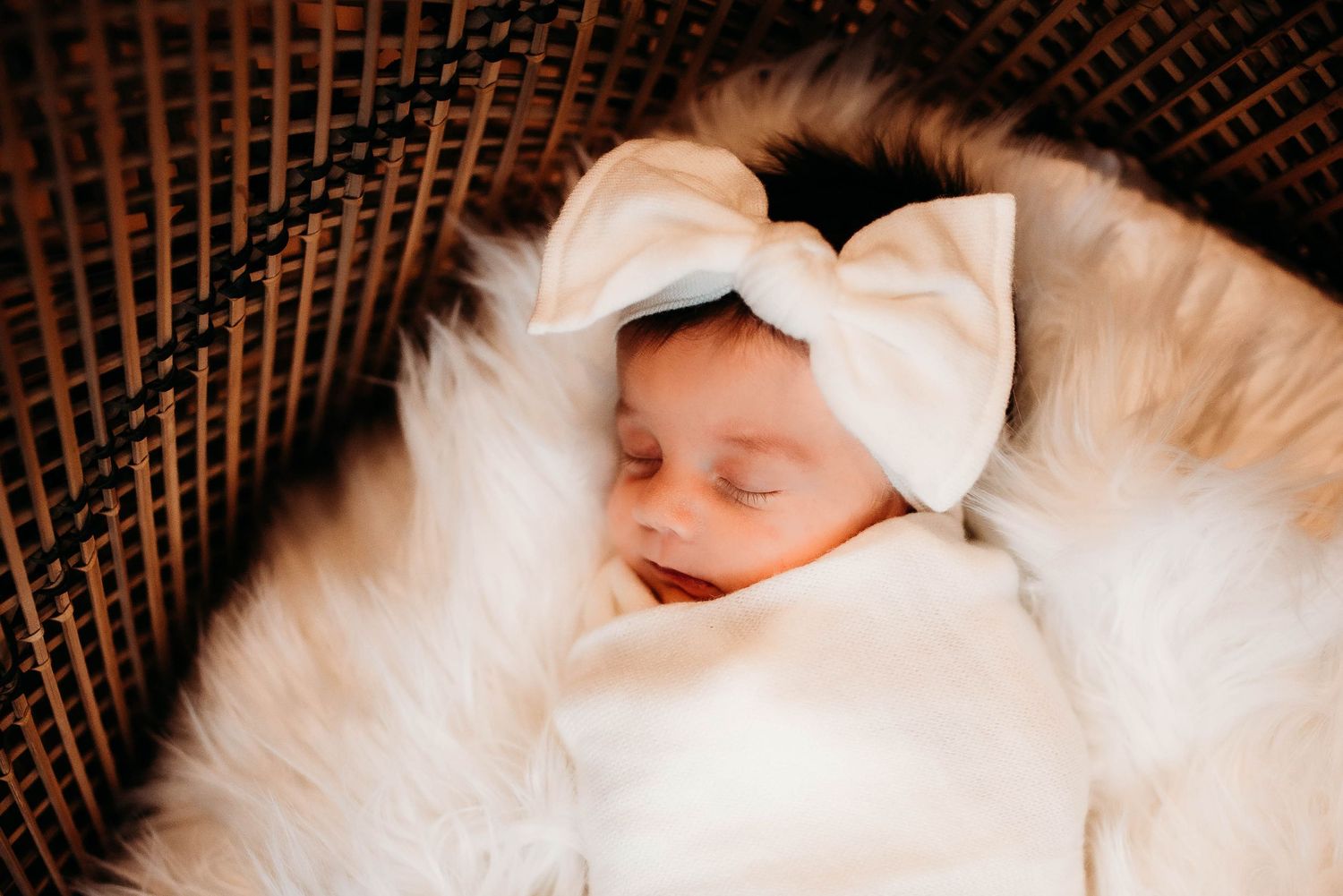 A sleeping newborn wrapped in white fabric against a textured brown background.