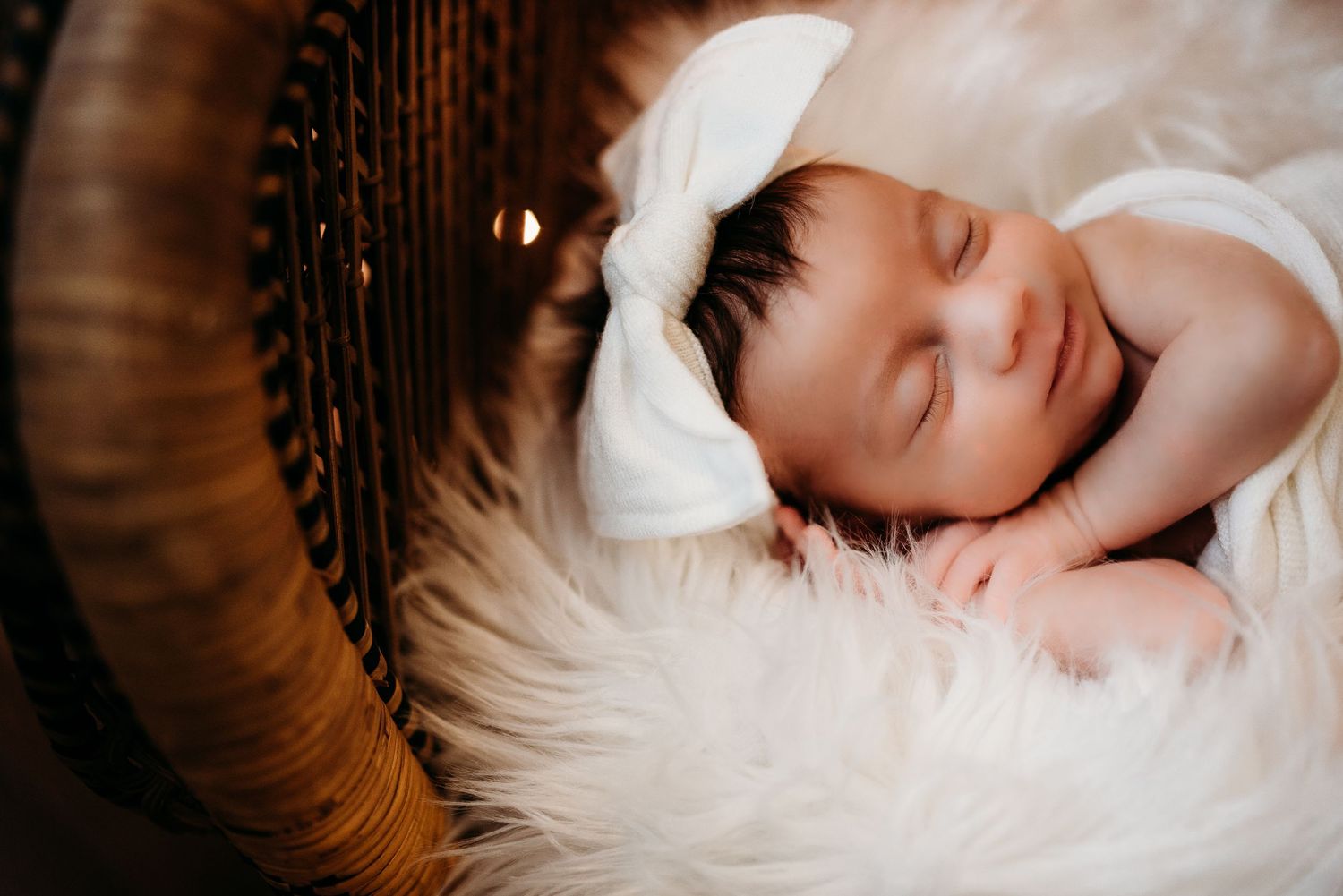 Newborn photography with baby sleeping on white fur backdrop.
