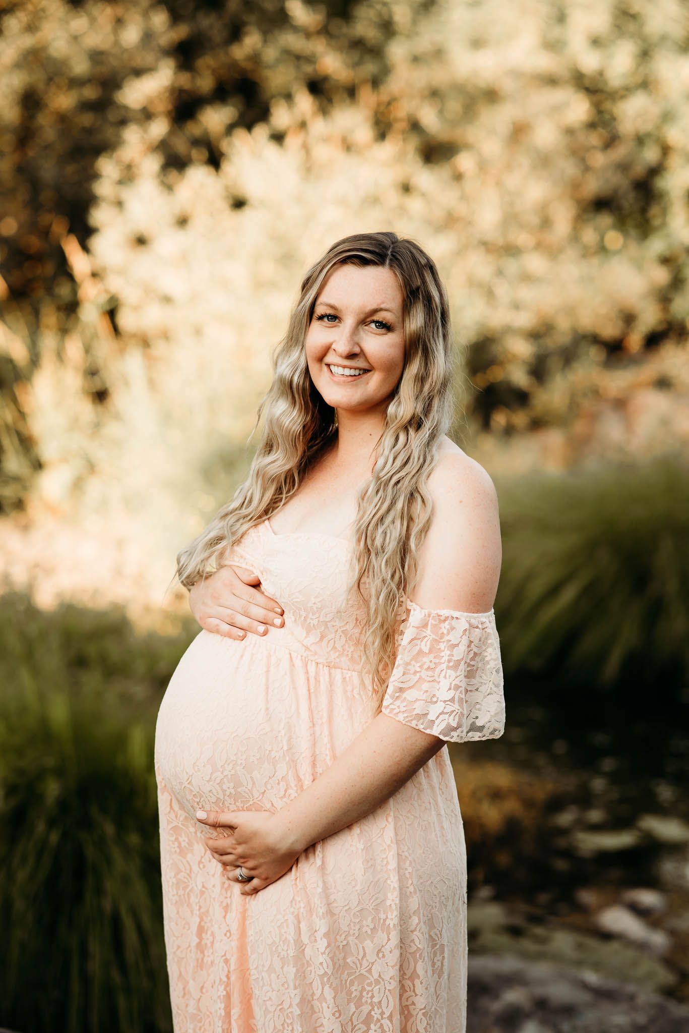 A maternity photoshoot in a peach lace dress during golden hour outdoors.