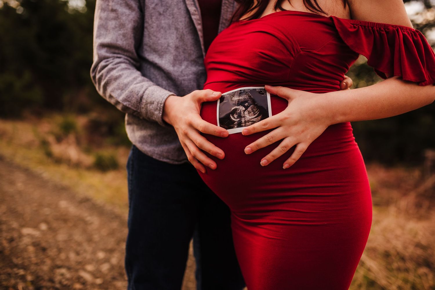 Maternity photography showing hands cradling baby bump in red dress.