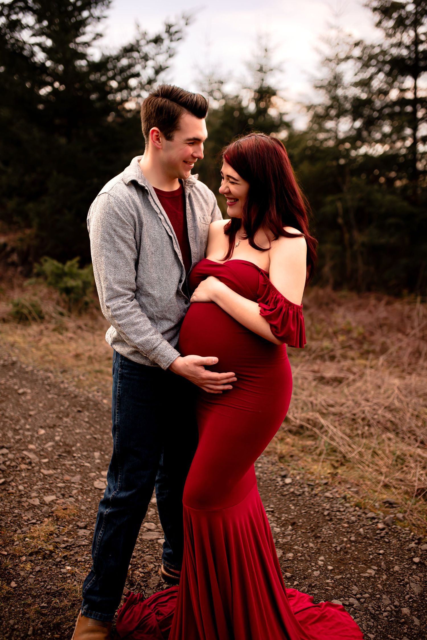 A couple embraces tenderly in a forest setting, with the woman wearing a flowing red dress.
