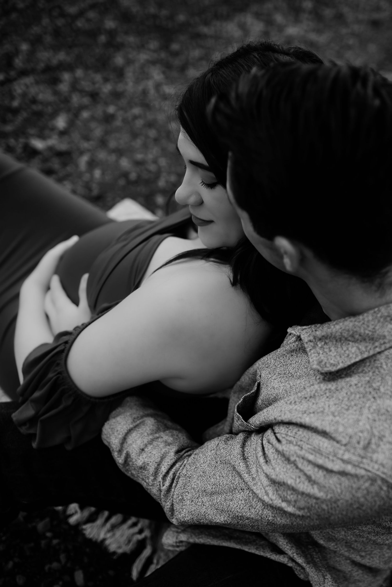 A romantic black and white photo of a couple lying close together outdoors.