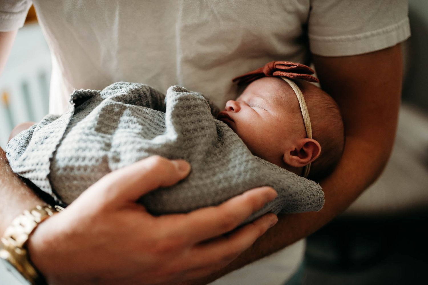 Tender moments of parent cradling sleeping newborn baby wrapped in gray blanket.