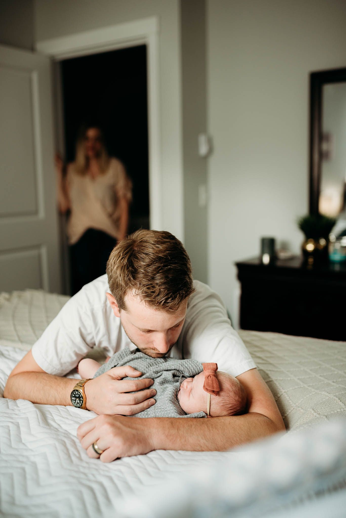 An intimate family moment captured on a white bed in natural light.