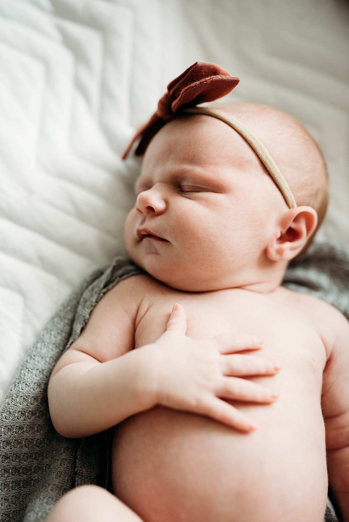 Sleeping newborn baby wearing brown headband lying on soft gray blanket.