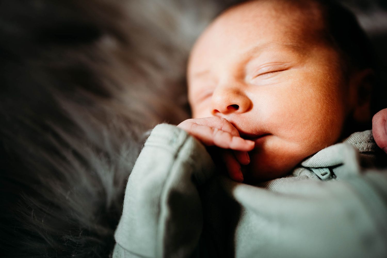 Peaceful sleeping newborn baby in mint green outfit captured in moody lighting.