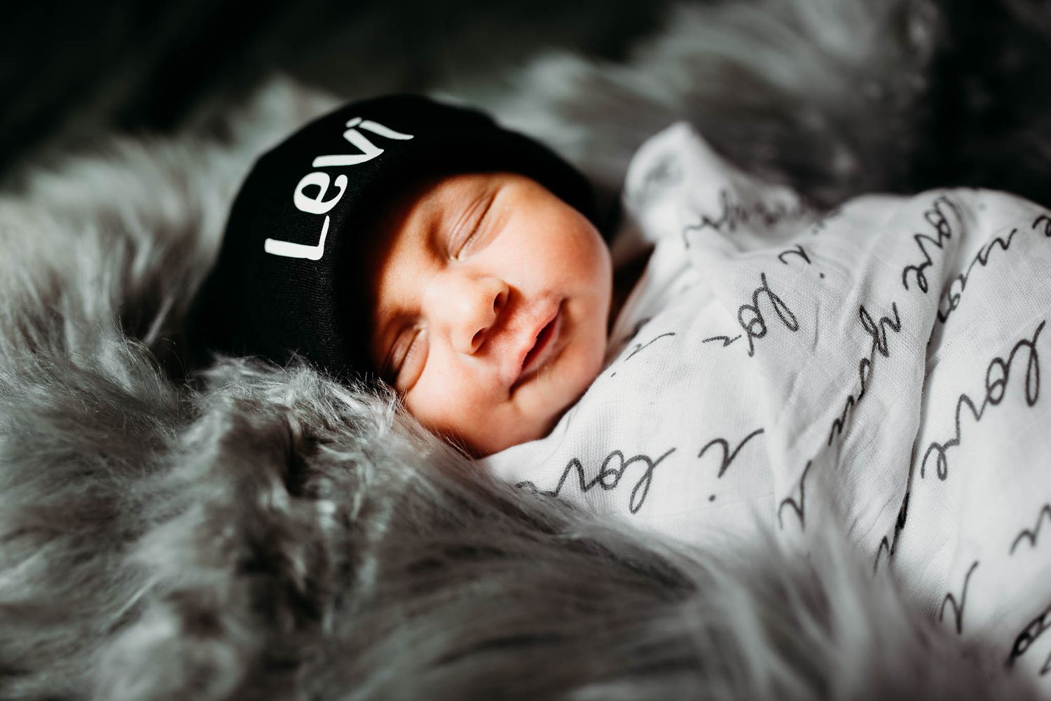 Sleeping infant resting on patterned fabric in dramatic black and white lighting.