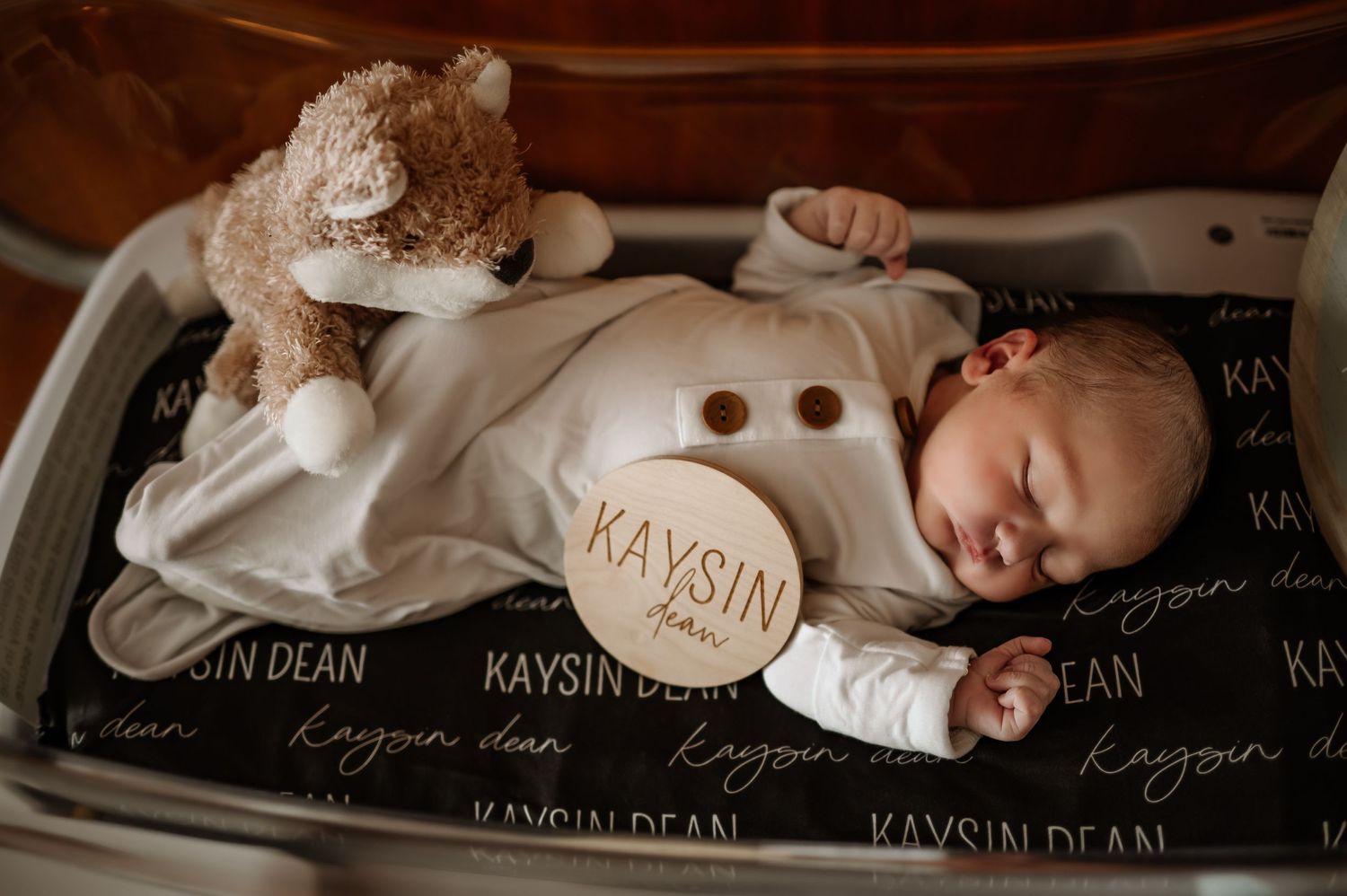 Sleeping newborn photographed on custom name-printed dark fabric backdrop.