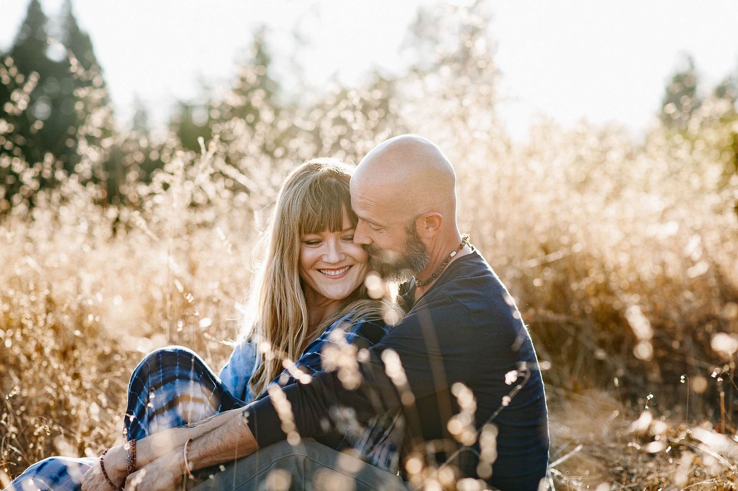 Couple sharing tender moment in sunlit golden field with tall grass.