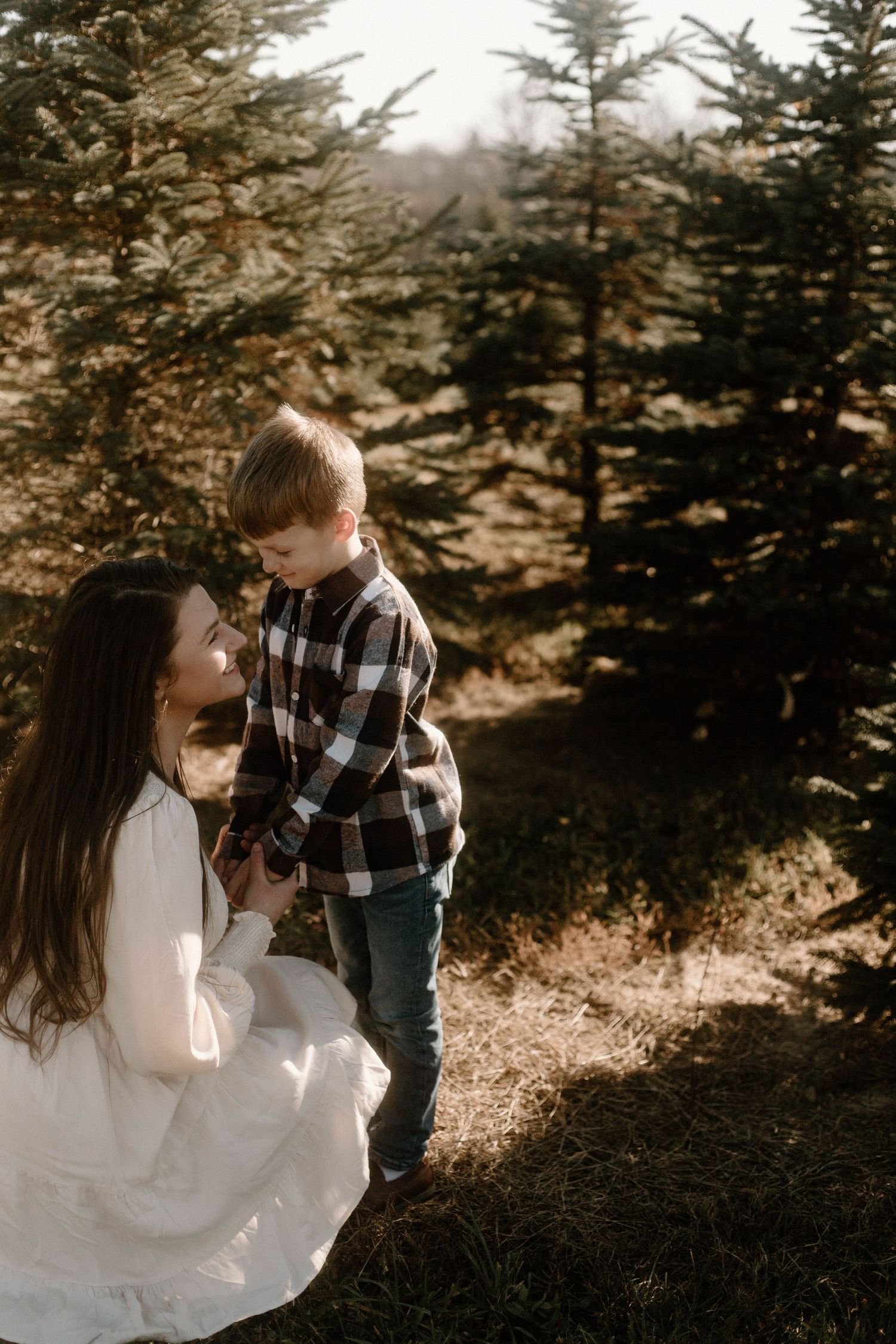Mother and child share intimate moment among pine trees in sunlit forest.