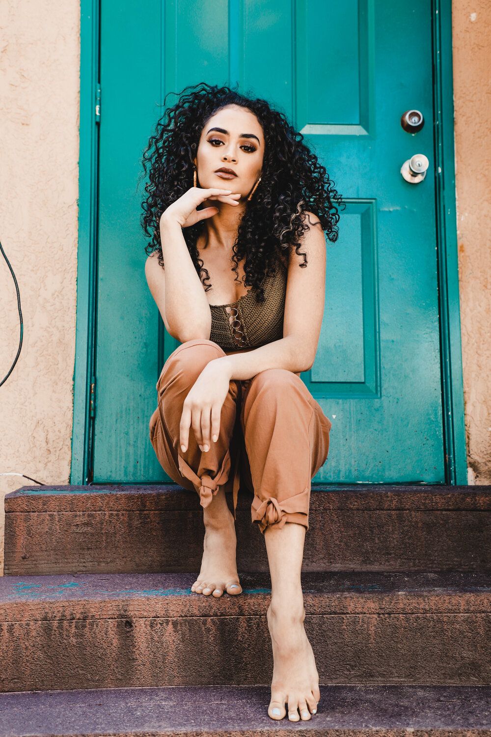 Portrait against a vibrant turquoise door showing casual style and natural curly hair.