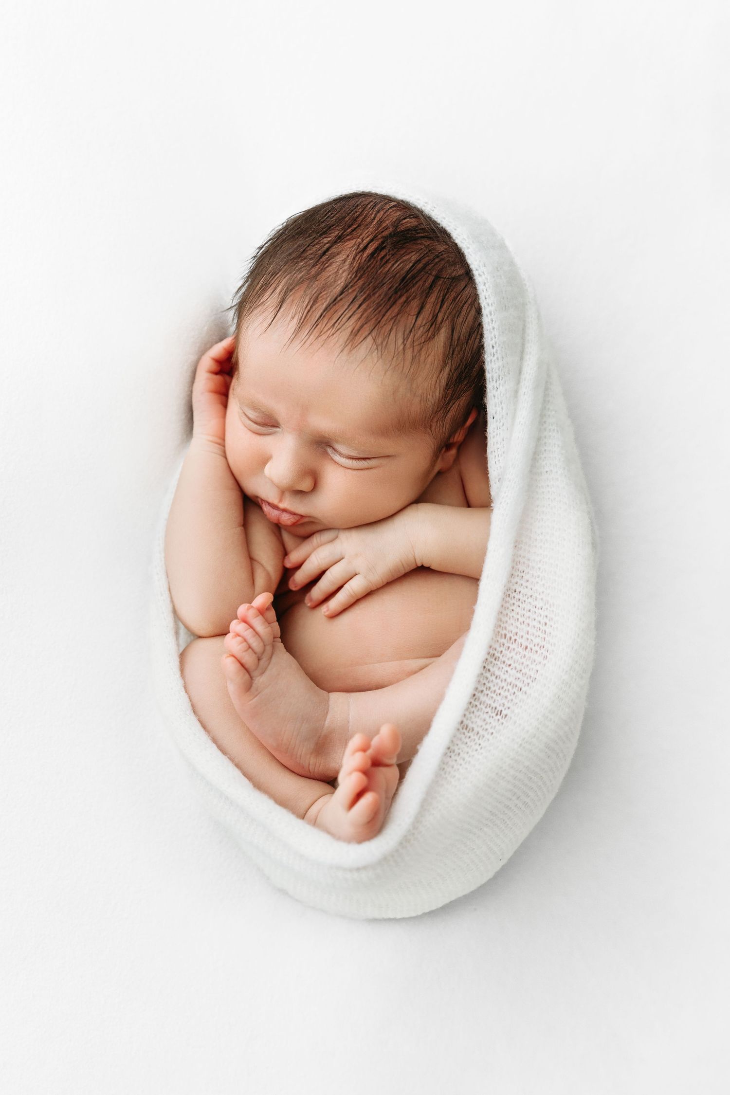 Newborn wrapped in white blanket, fetal position.