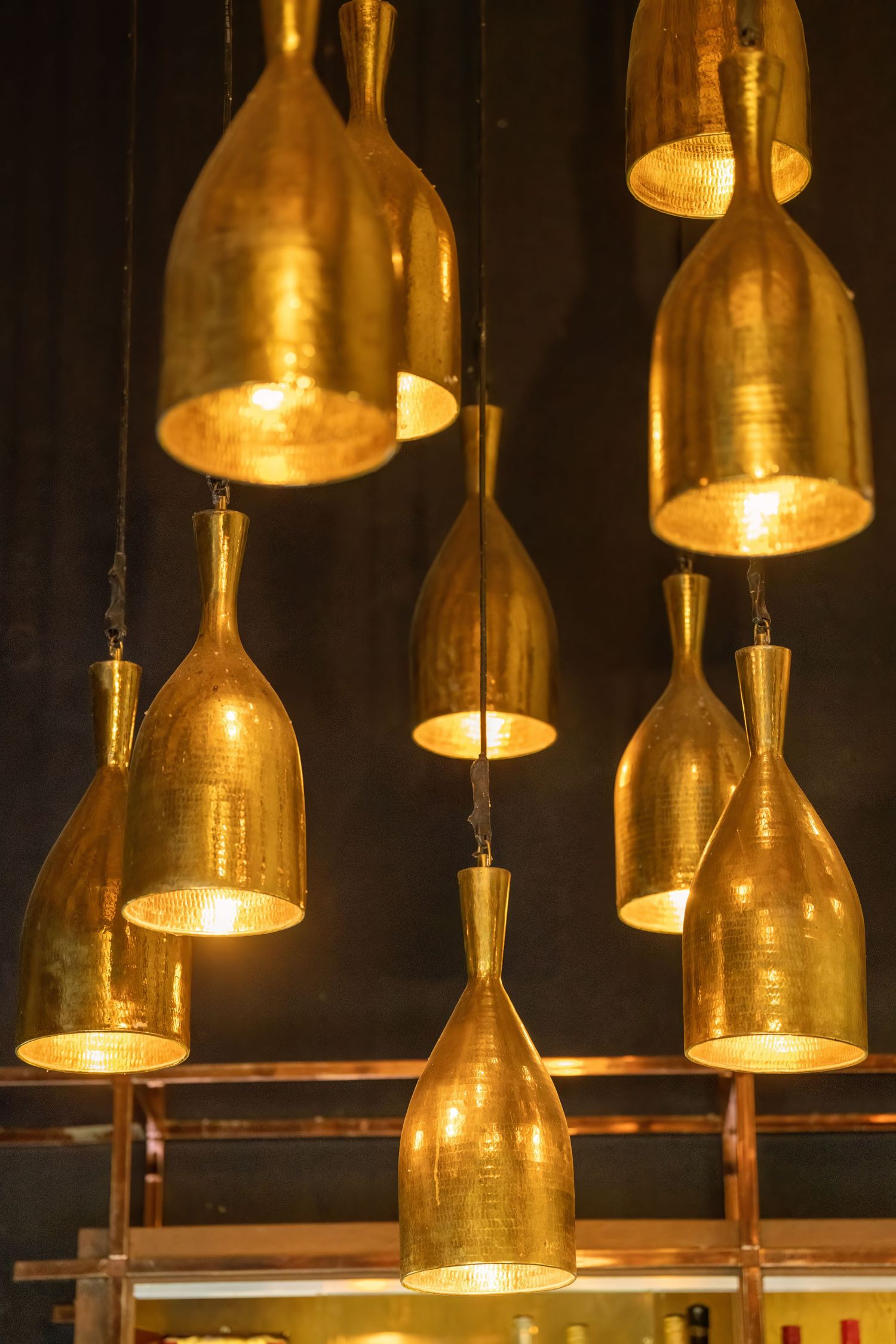 Artistic lighting installation made from illuminated golden wine bottles hanging from the ceiling.
