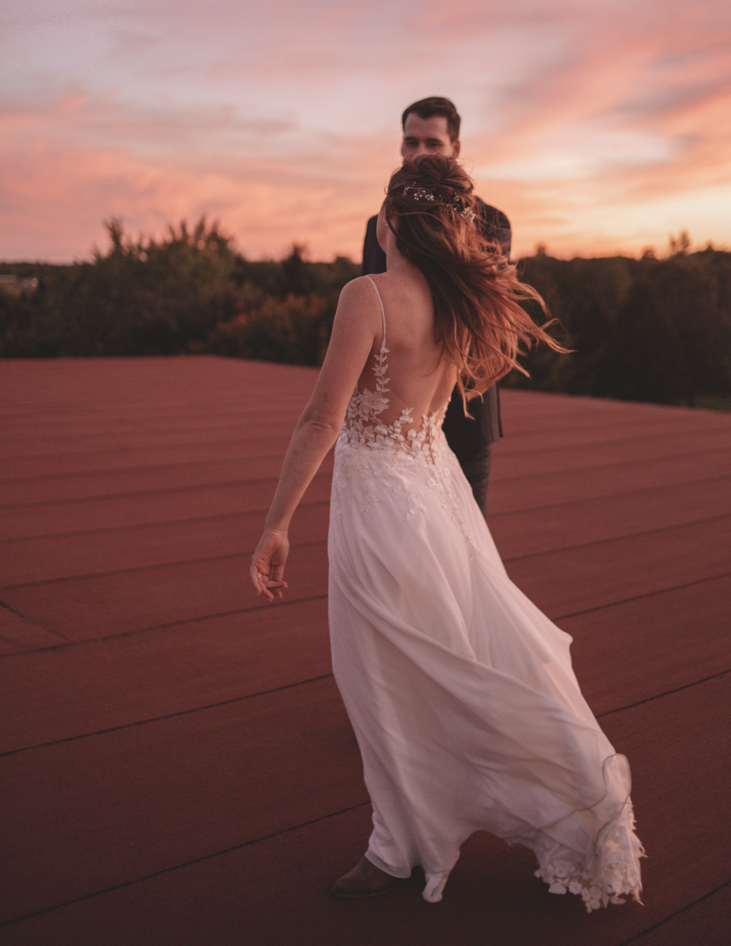 Romantic sunset portrait of couple dancing with flowing lace wedding dress.