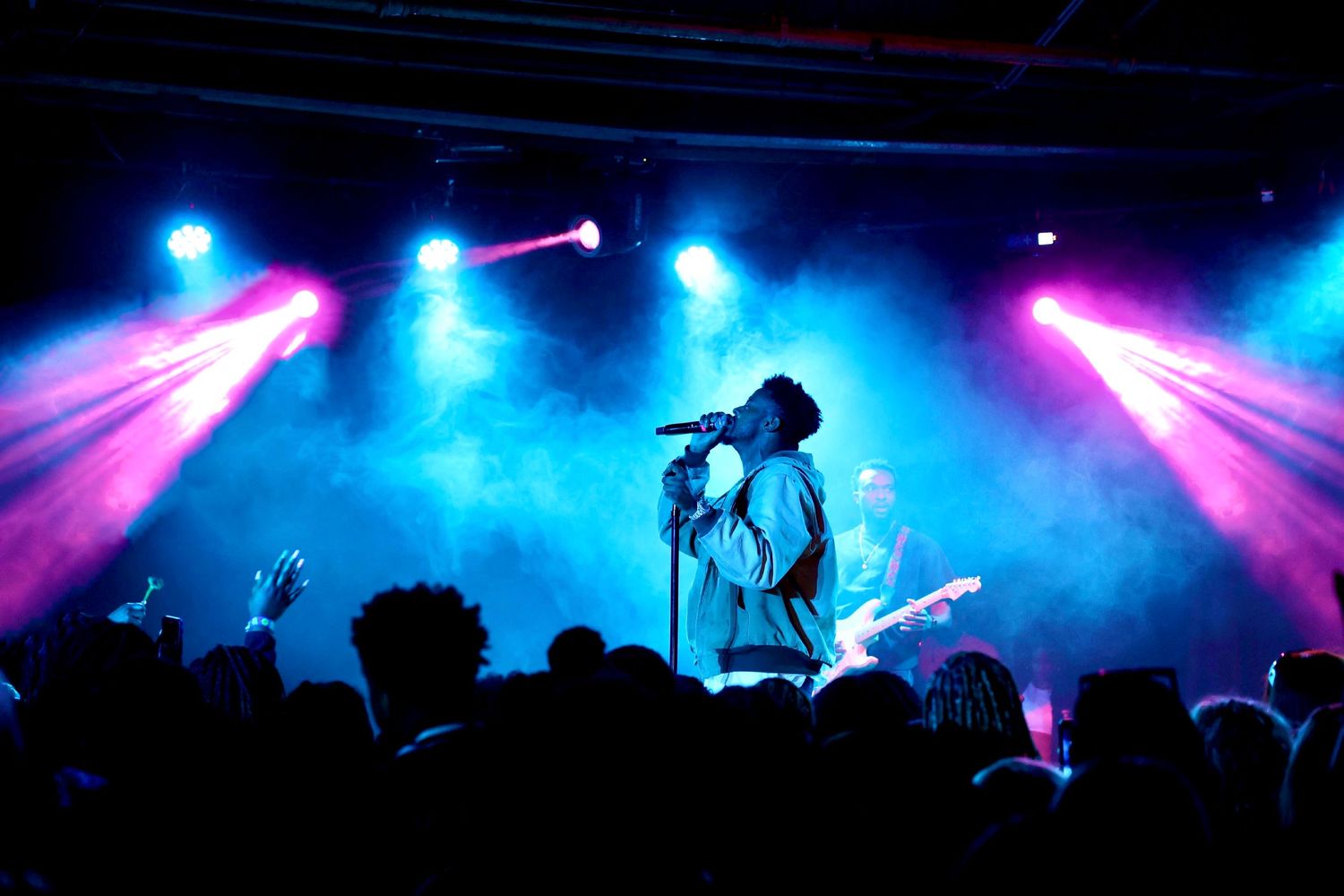 Silhouetted performer on stage with colorful pink and blue lighting effects during concert.