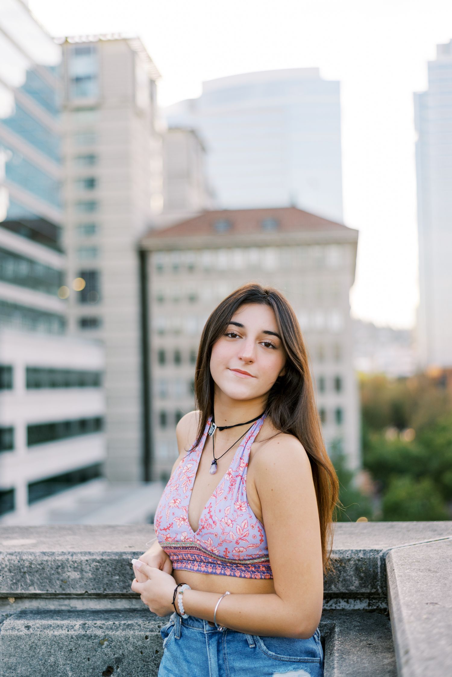 Young woman in purple crop top poses against urban cityscape backdrop.