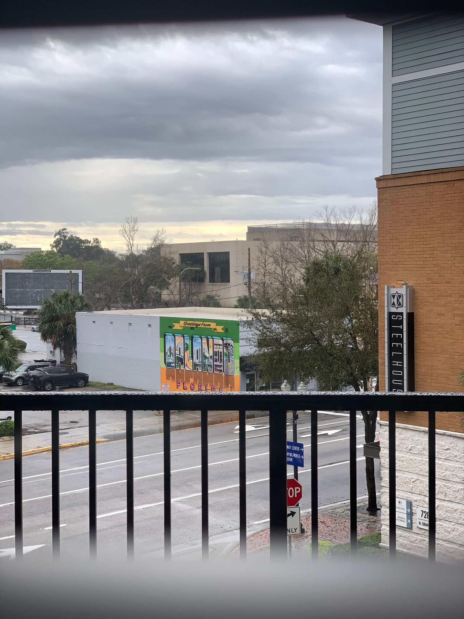 Urban parking lot view from a balcony with brick buildings and cloudy sky in the background.