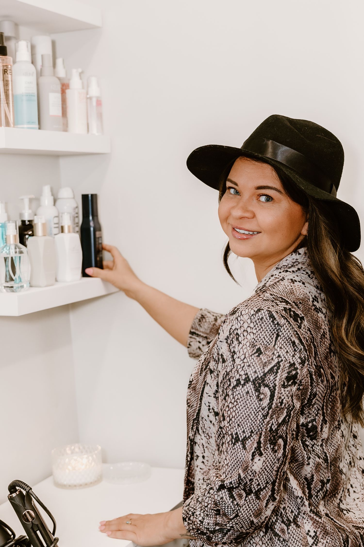 A hairstylist reaching for products on white floating shelves in a modern salon.