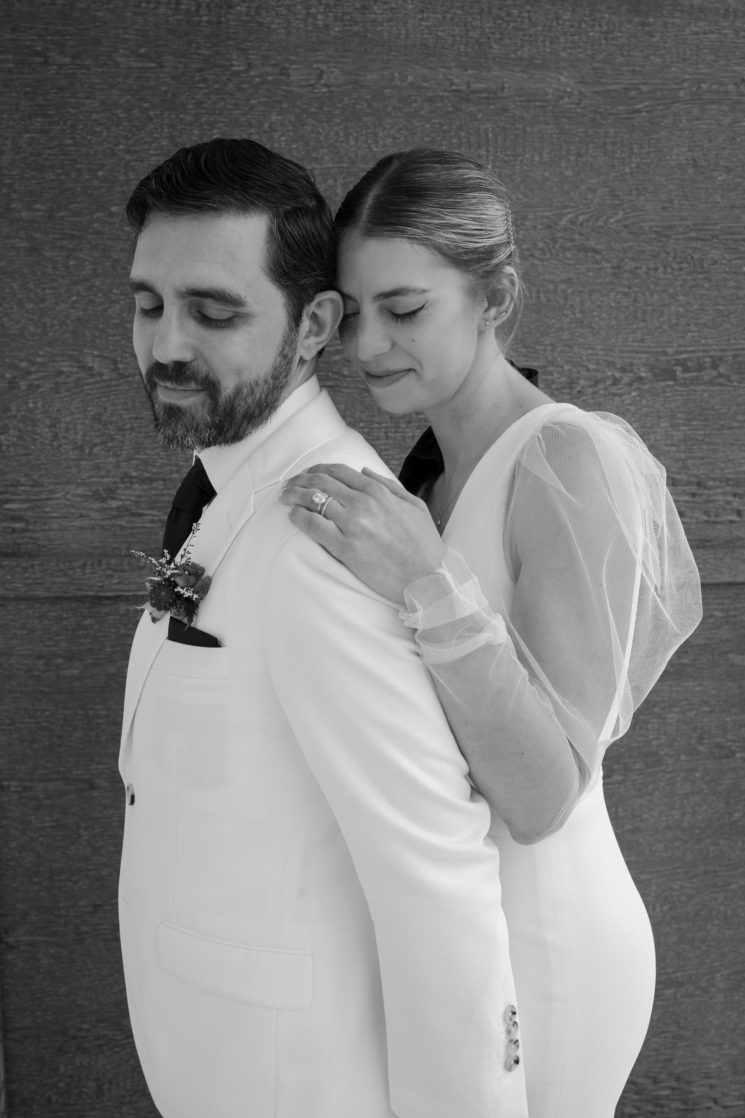 Elegant black and white portrait of newlyweds sharing an intimate moment against textured wall.