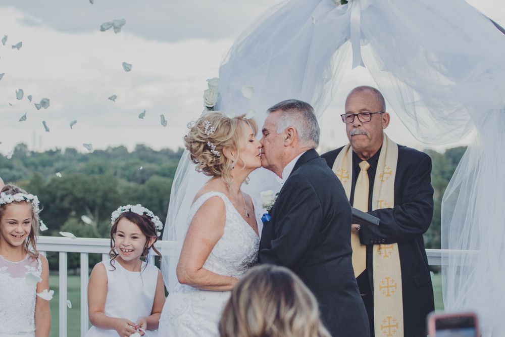 Wedding ceremony guests gather outdoors under a white tent.